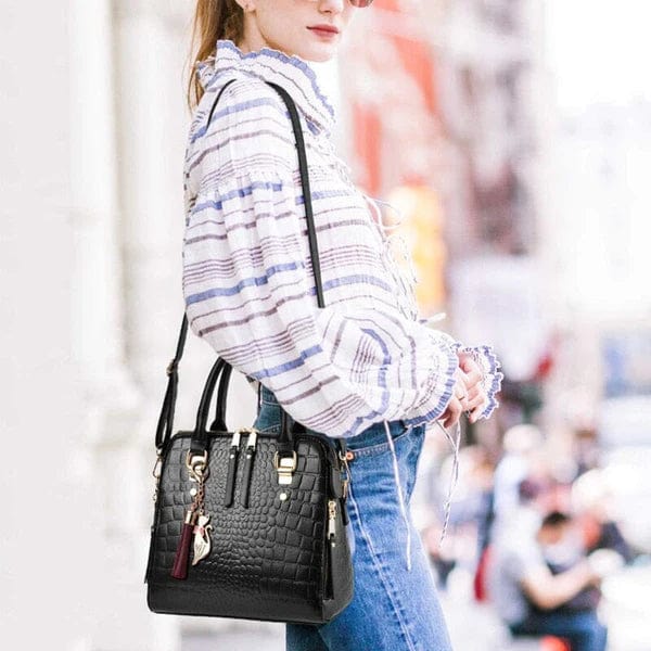 Woman in striped blouse and jeans carrying black crocodile leather handbag with gold hardware and tassel charm