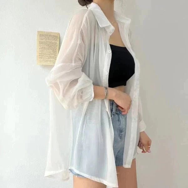 Woman wearing white sheer lightweight sun protection shirt open over black crop top and denim shorts