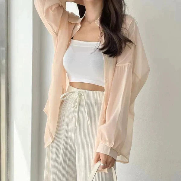 Woman wearing lightweight sun protection shirt in beige over white crop top with pleated drawstring pants