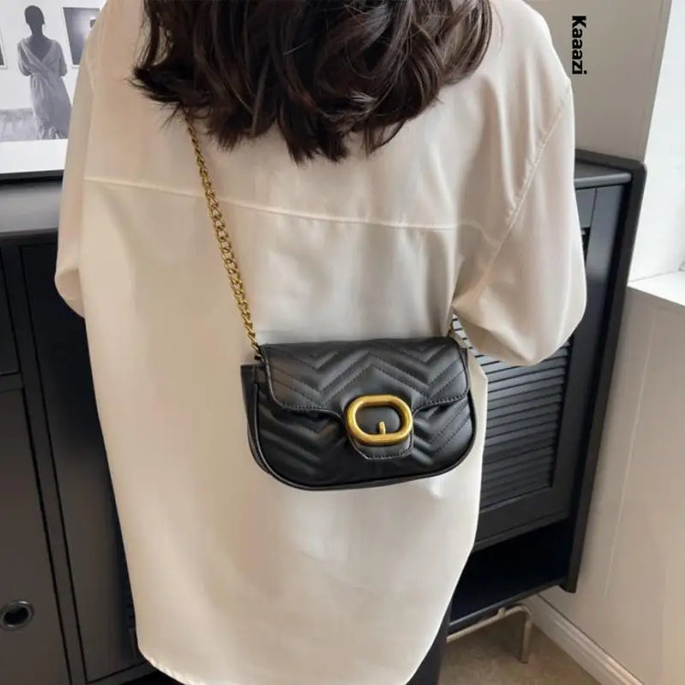 Woman wearing a black quilted crossbody with gold chain and buckle luxury minimalist leather bag over white blouse
