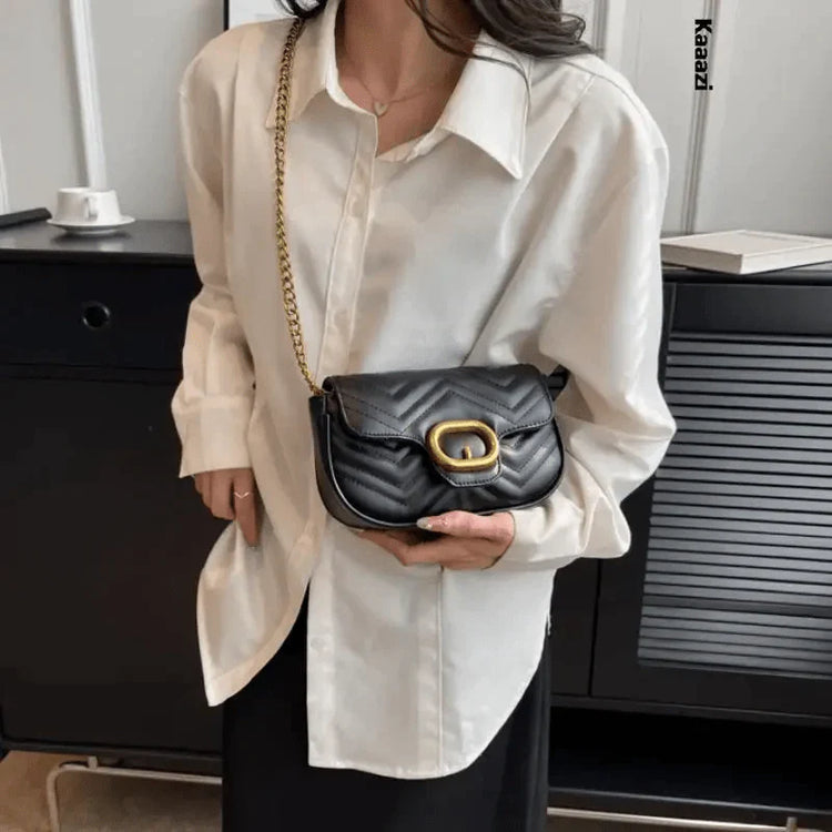 Woman in white blouse holding a black quilted luxury minimalist leather bag with gold chain strap and oval buckle