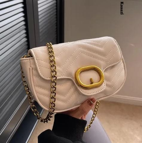 Cream quilted shoulder purse with gold chain strap and oval hardware held in hand luxury minimalist leather bag