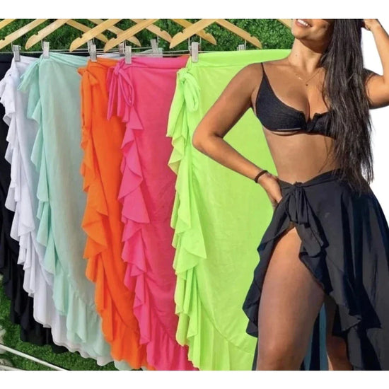 Model wearing black summer beach wrap skirt with high slit beside colorful ruffled wrap skirts on hangers
