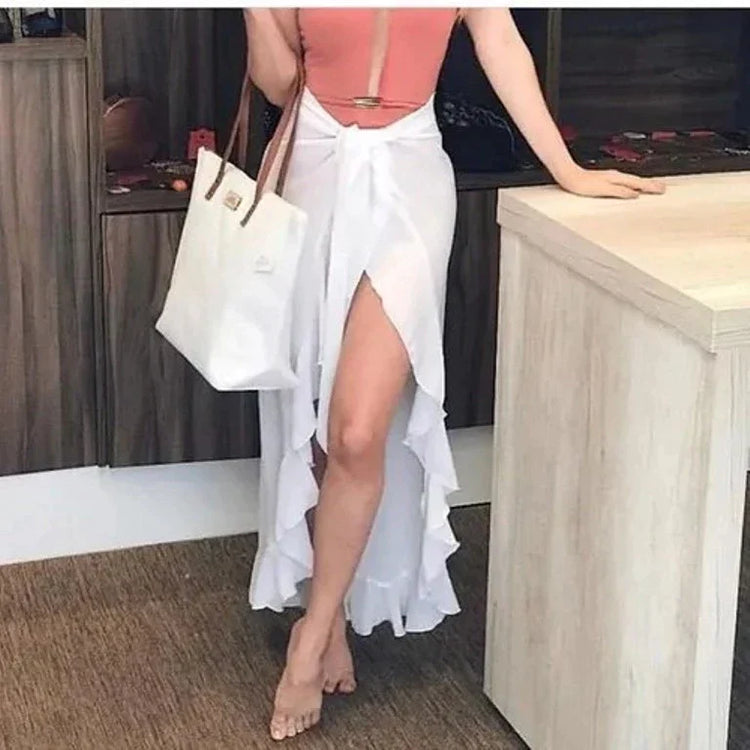 White ruffled summer beach wrap skirt with high slit styled with pink swimsuit and white tote bag